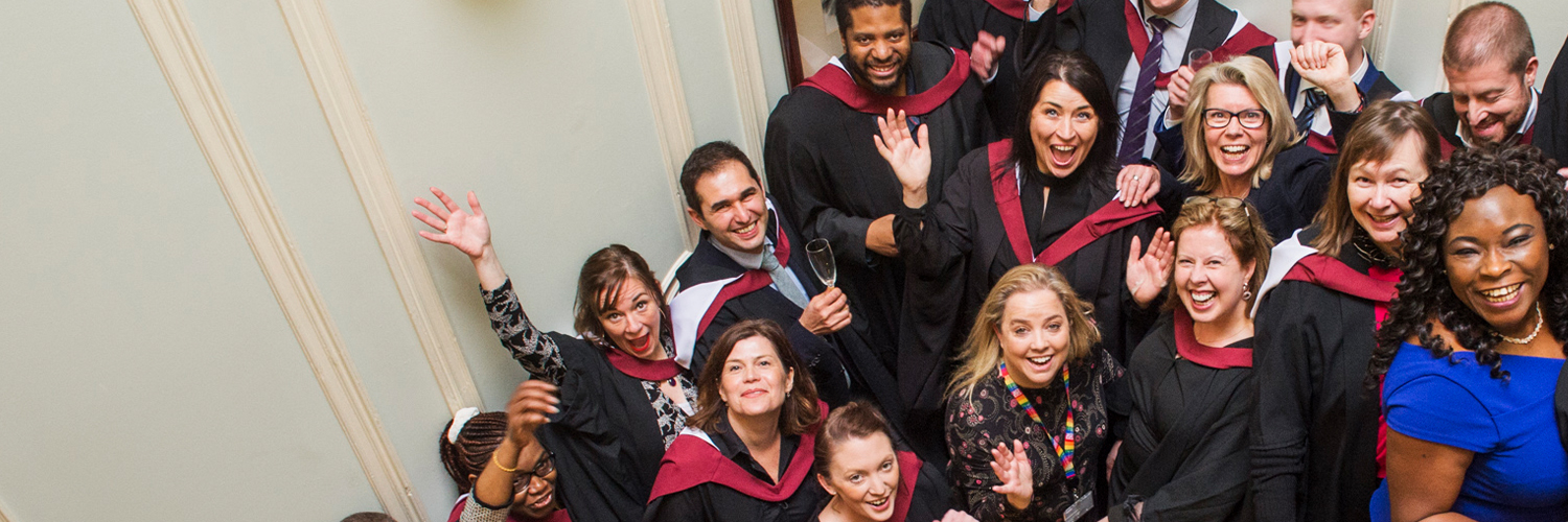A large diverse group of people wearing graduation gowns and smiling at the camera